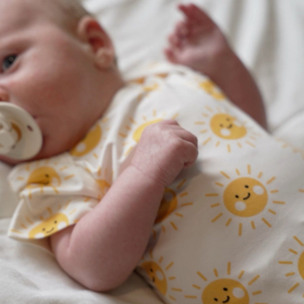 Baby wearing a onesie with sun patterns on a white blanket