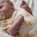 Baby wearing a onesie with sun patterns on a white blanket