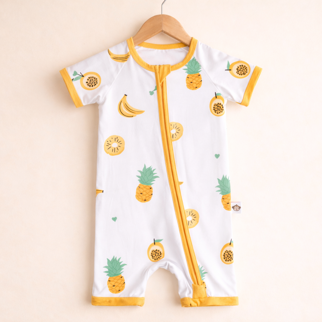 Baby romper with pineapple and banana pattern on a hanger against a beige background
