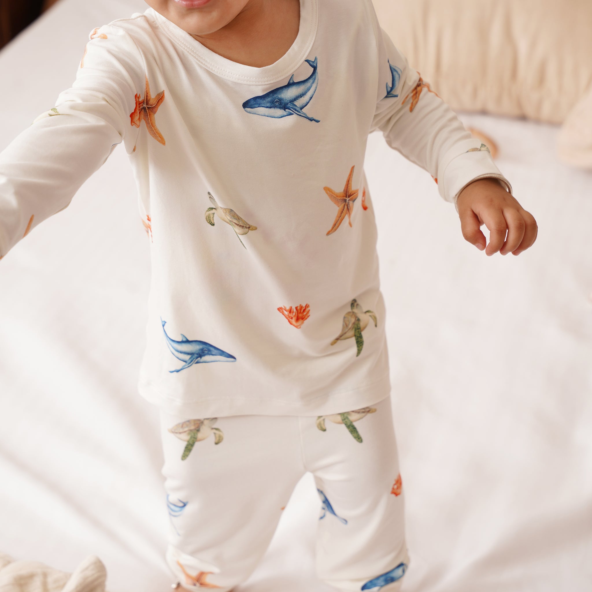 Child wearing a white long-sleeve shirt and pants with colorful animal prints on a light background.