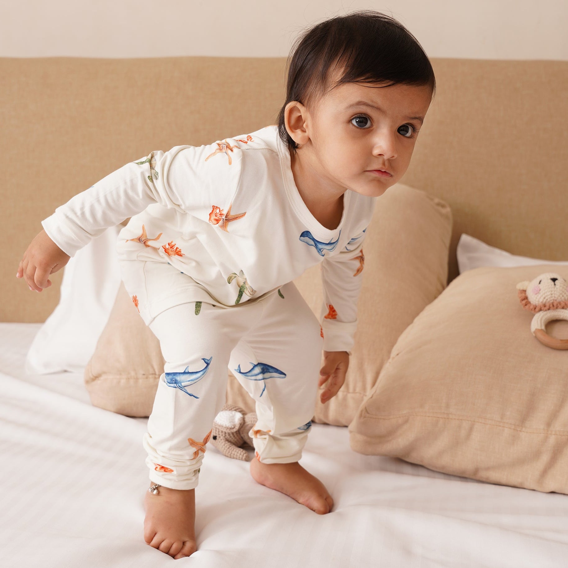 Baby in pajamas standing on a bed with a neutral background