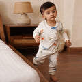 Baby in a white bamboo outfit with colorful designs standing in a bedroom.