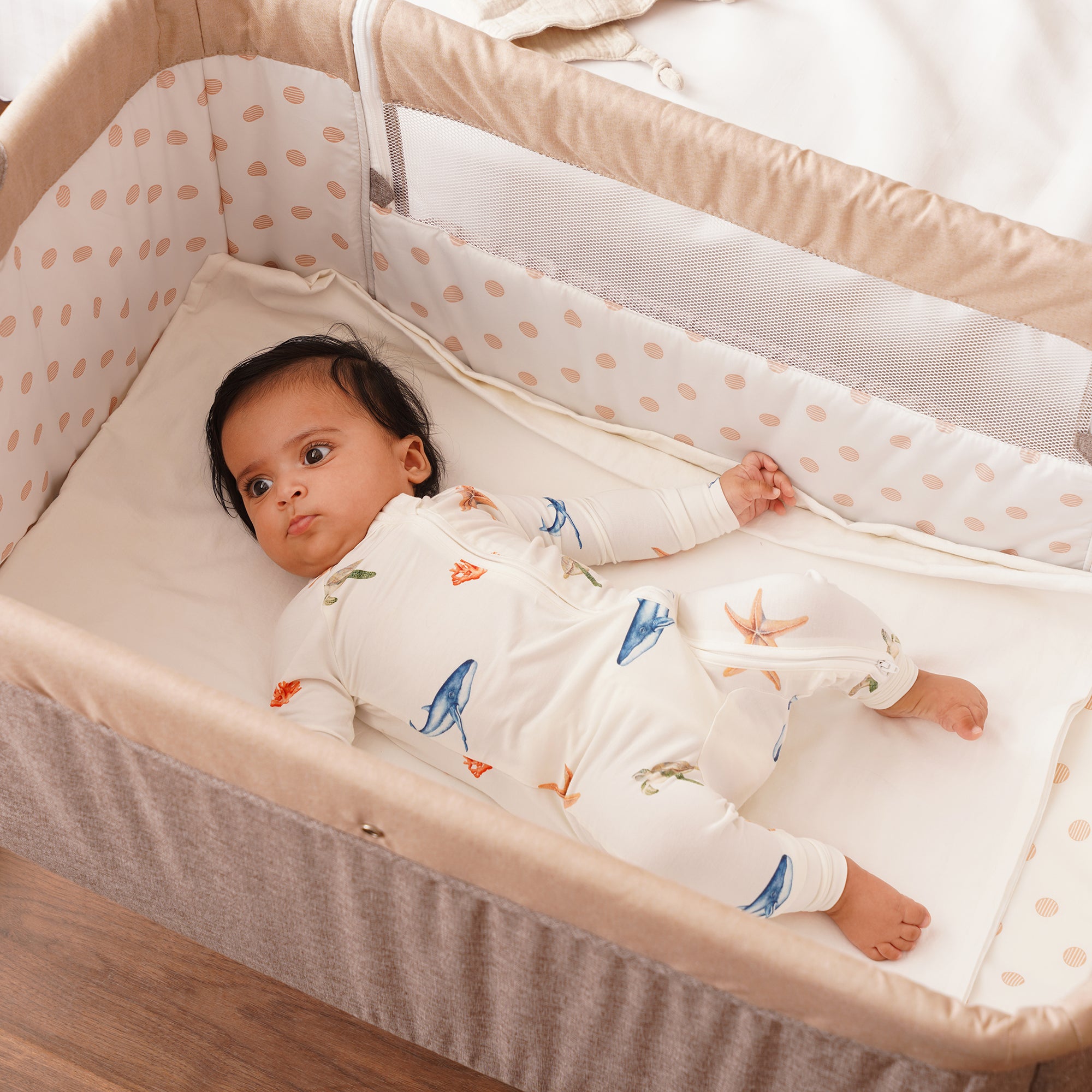 Baby lying in a crib with a polka dot bumper, wearing bamboo onesie