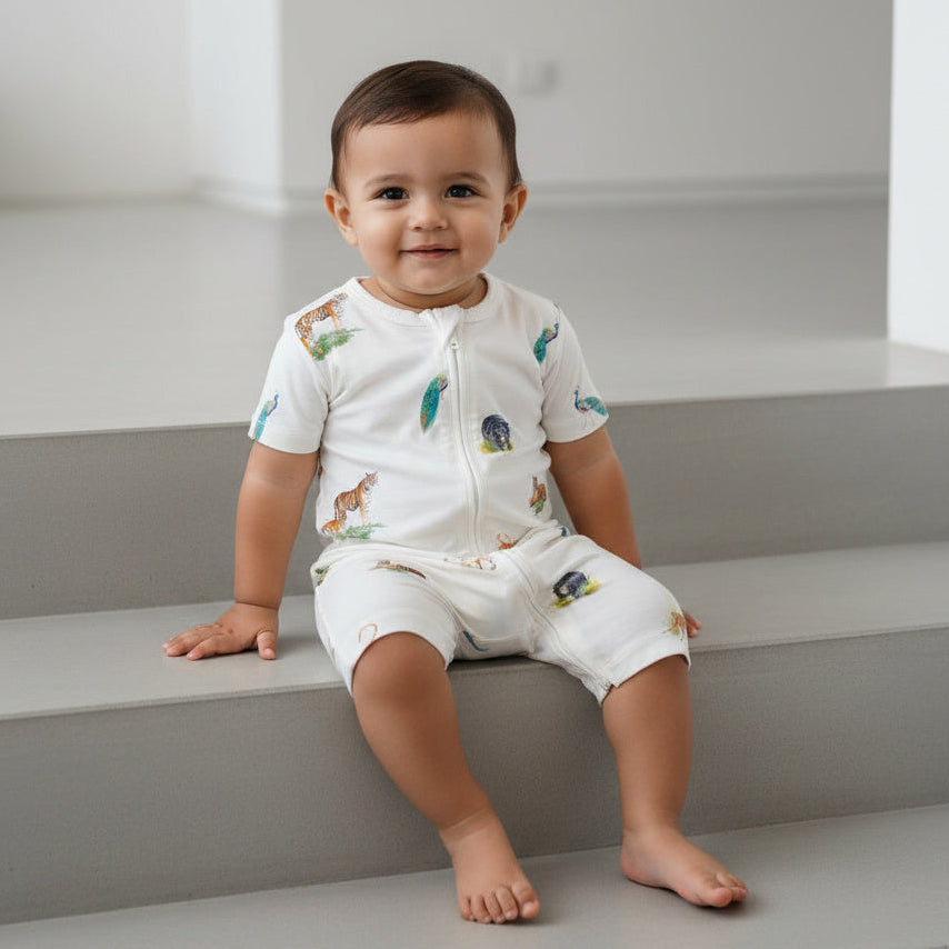 Baby sitting on a staircase wearing a white onesie with animal prints.