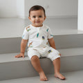Baby sitting on a staircase wearing a white onesie with animal prints.