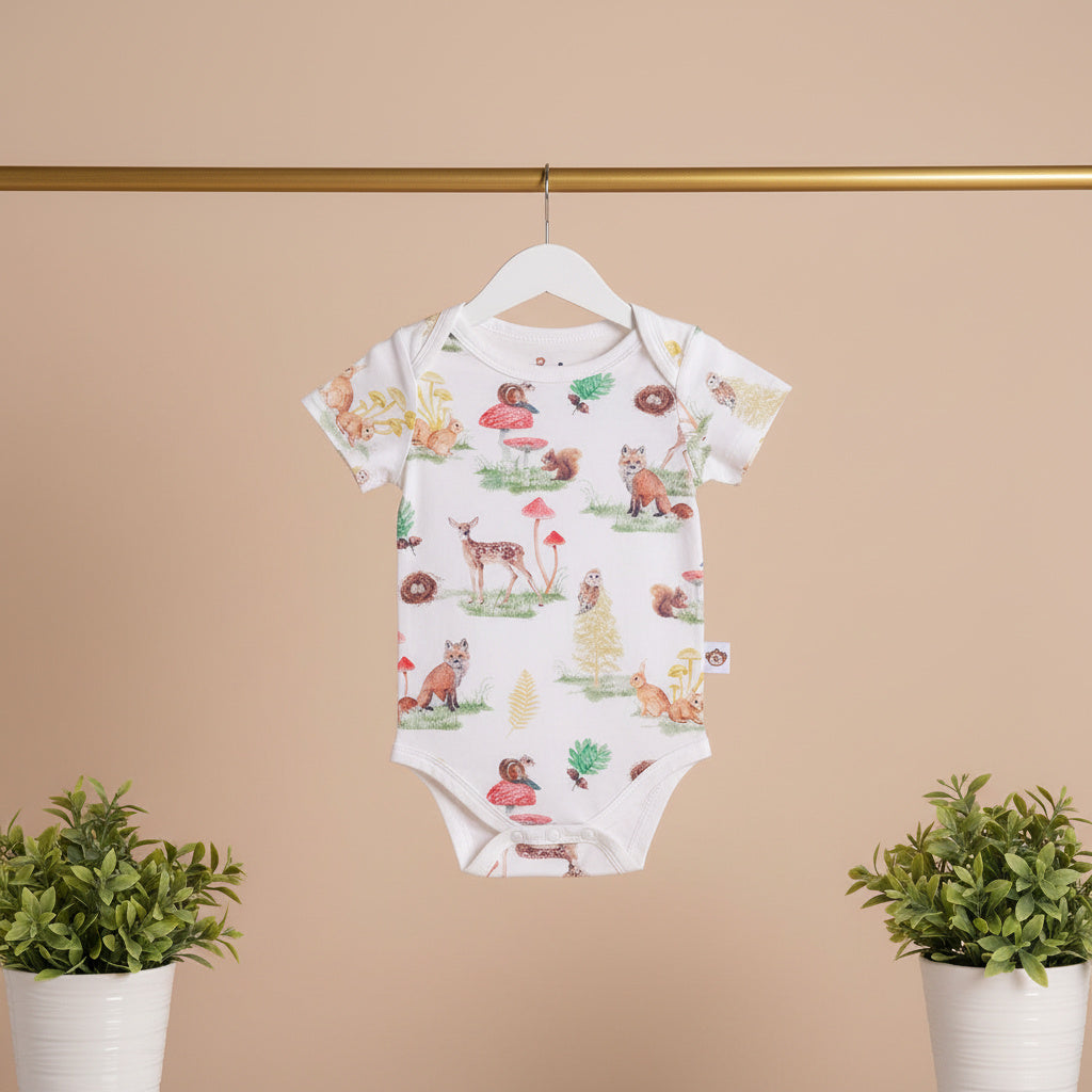 Baby onesie with nature-themed print on a hanger against a beige wall with plants.